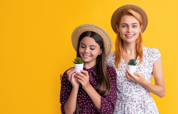 Positive mother and daughter with plant in pot on yellow background