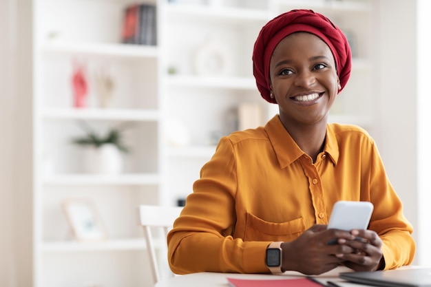 Positive muslim black woman using mobile phone and smiling