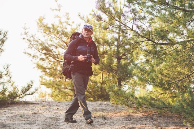 Uomo anziano positivo che fotografa il paesaggio nella foresta