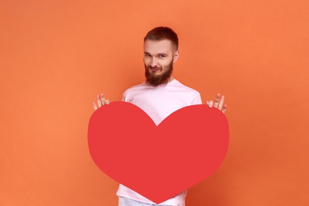 Positive optimistic man holding big red heart expressing positive romantic emotions