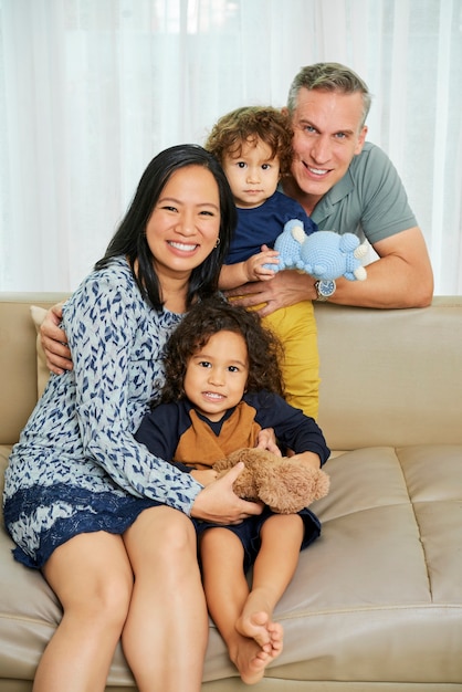 Positive parents and their two sons resting on sofa at home and smiling at camera