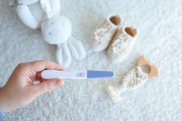 Positive pregnancy test in hand against the background of children's clothing