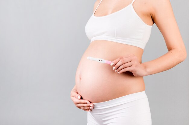 Positive pregnancy test with two stripes against pregnant woman