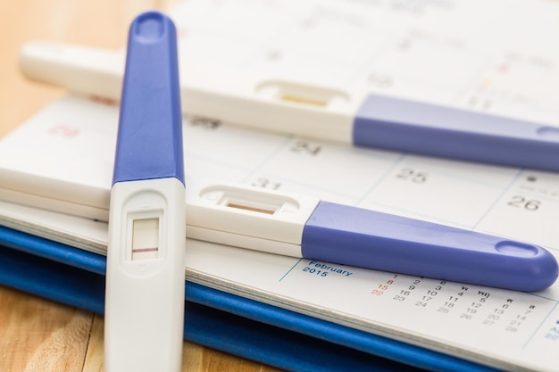 positive pregnant tester on calendar and wooden table close up