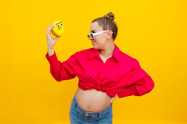 Positive pregnant woman eating donuts wearing pink shirt isolated on yellow background happiness from pregnancy while expecting a child high quality photo harmful food during pregnancy