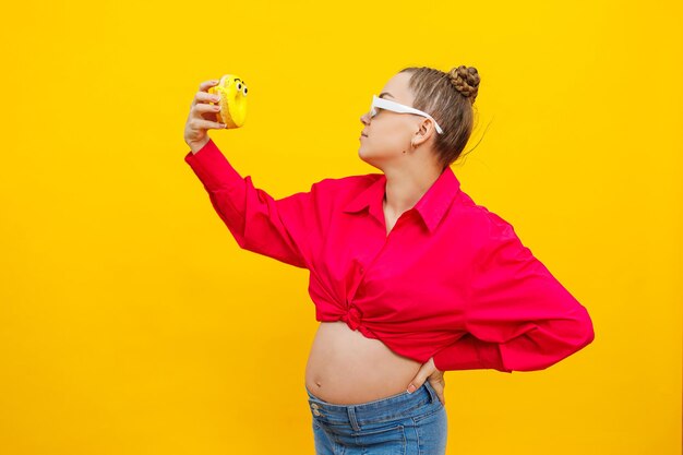 Positive pregnant woman eating donuts wearing pink shirt isolated on yellow background Happiness from pregnancy while expecting a child High quality photo Harmful food during pregnancy