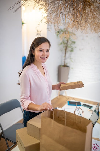 Positive pretty woman smiling while preparing presents for Christmas