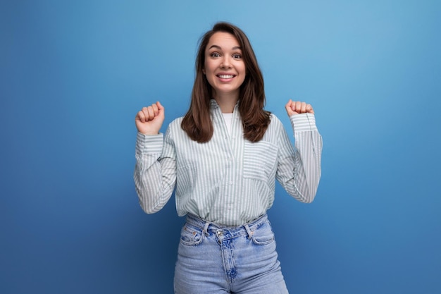 Positive pretty young brunet female adult in striped shirt and jeans isolated on plain background