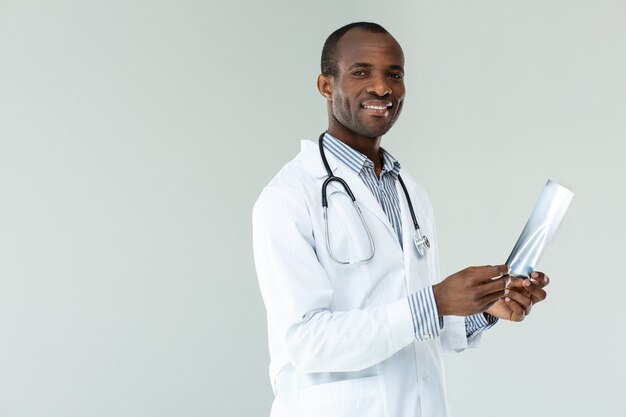 Positive professional doctor holding x- ray scan of chest against white wall