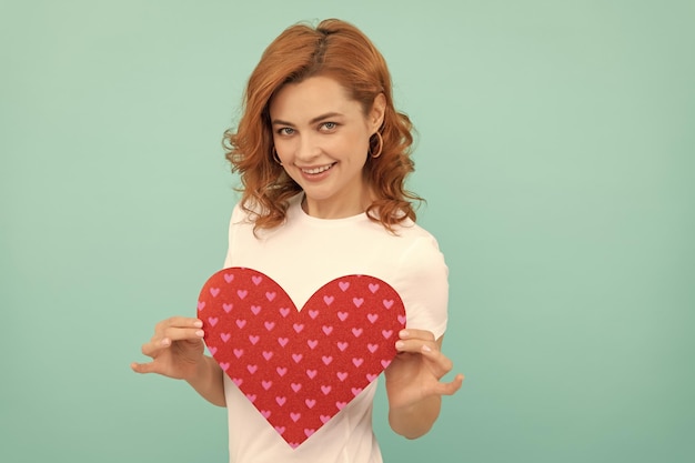 Positive redhead lady hold red heart on blue background