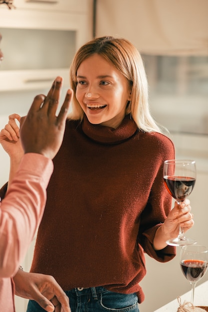 Foto positiva e rilassata giovane donna che sembra felice e ride mentre è in piedi con un bicchiere di vino e ha una macchia di farina sulla punta del naso