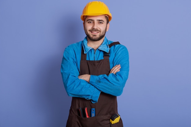 Хороший ремонтник носит желтый защитный строительный шлем, рубашку и коричневый фартук, готовый к ремонту дома.