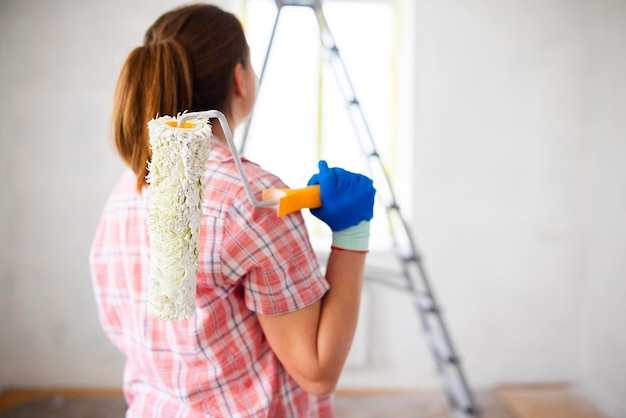 Positive satisfied woman holding dirty roller after painting walls in room