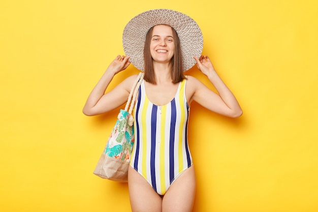 Positive satisfied woman wearing swimsuit isolated on yellow background relaxing at beach smiling with cheerful expression good rest near sea