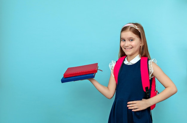 A positive schoolgirl girl is holding books and smiling.