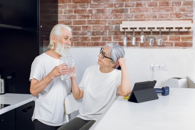 Positive senior couple drinking water after workout at home