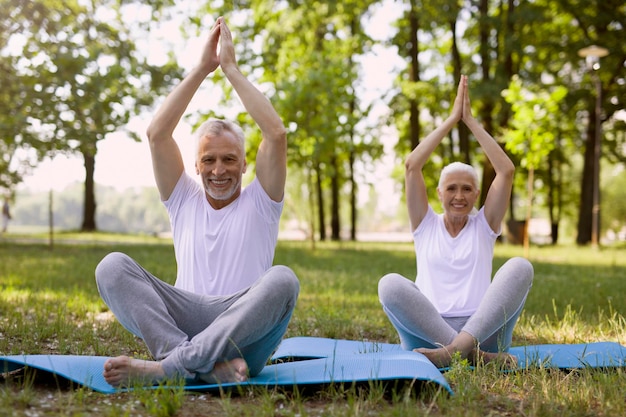 Photo positive senior couple keeping their hands up and crossing their legs while meditating together