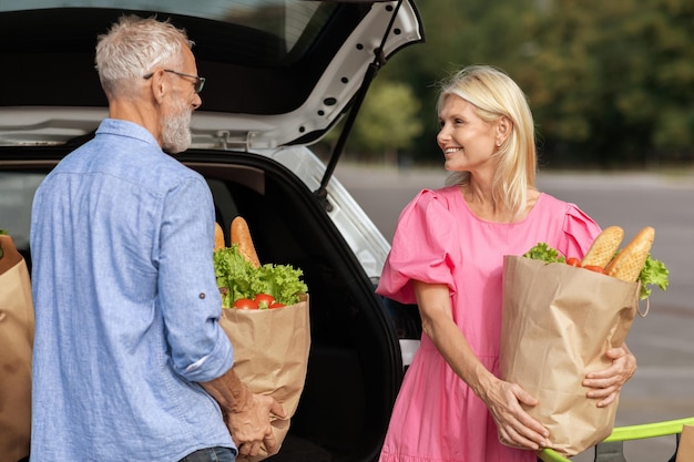 positive senior couple putting grocery packages in auto