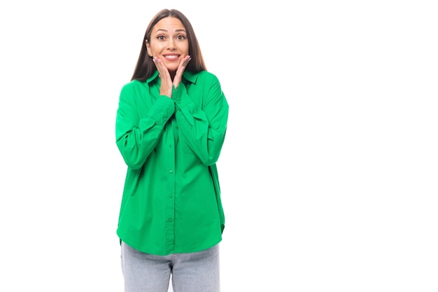 Giovane donna castana europea esile positiva con trucco in camicia verde su fondo bianco con la copia