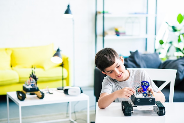 Photo positive smart schoolboy enjoying engineering while constructing a modern robot at home