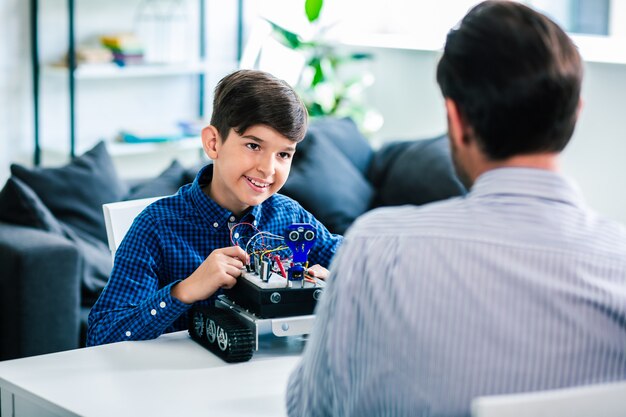 Positive smart schoolboy testing his robotic device while resting with his father