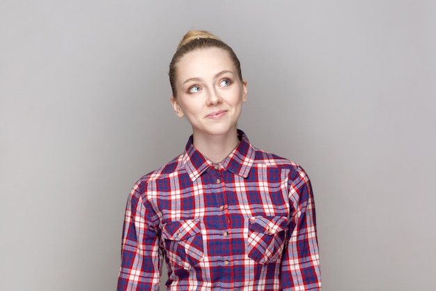 Positive smiling adorable woman with bun hairstyle looking away thinking about future dreaming