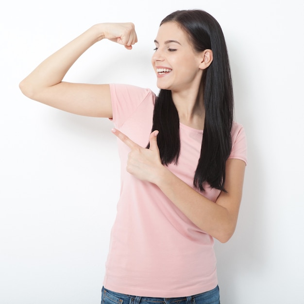 Positive smiling asian woman with dark hair, perfect smile, raises arms and shows biceps.