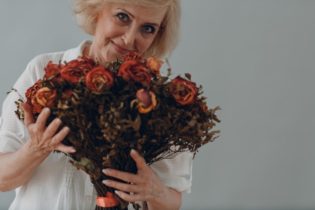 ポジティブな笑顔の年配の女性が手にバラの花の花束を保持します。