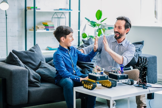 Positive smiling father and his ingenious son spending time on robotic technologies while resting at home