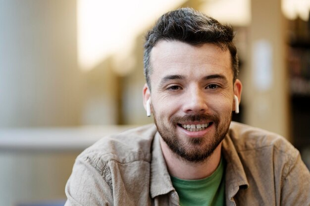 Positive smiling man in wireless headphones sitting looking at camera