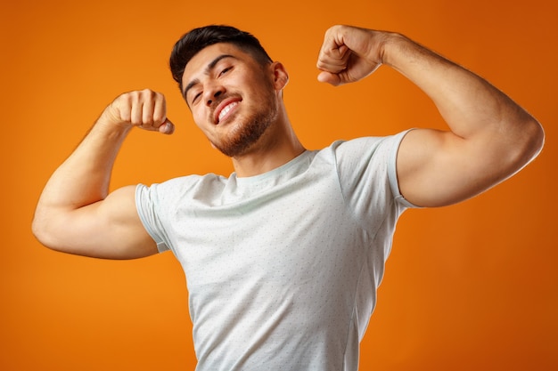 Photo positive smiling young man showing his strong arms against yellow background close up