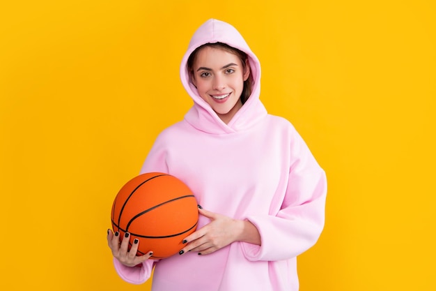 Positive sporty girl with basketball ball on yellow background