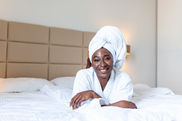 하루에 긍정적 인 시작. 목욕 가운에 침대에 누워 웃는 아프리카 젊은 여자.