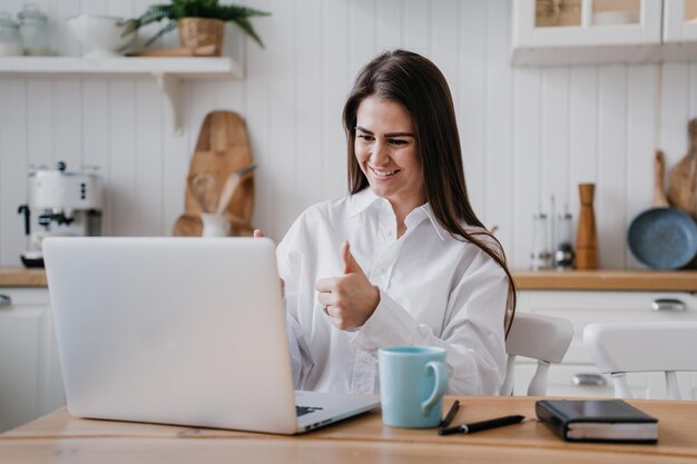 Foto studente positivo a casa che effettua una chiamata a distanza utilizzando il laptop che mostra il pollice sul gesto sorridente soddisfatto
