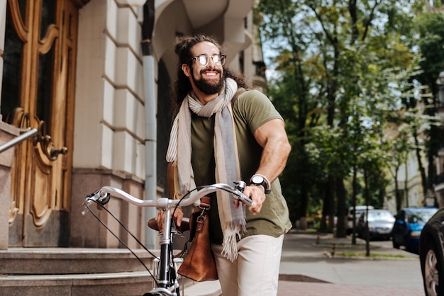 Positive stylish man wearing sunglasses while riding in the city on a bicycle