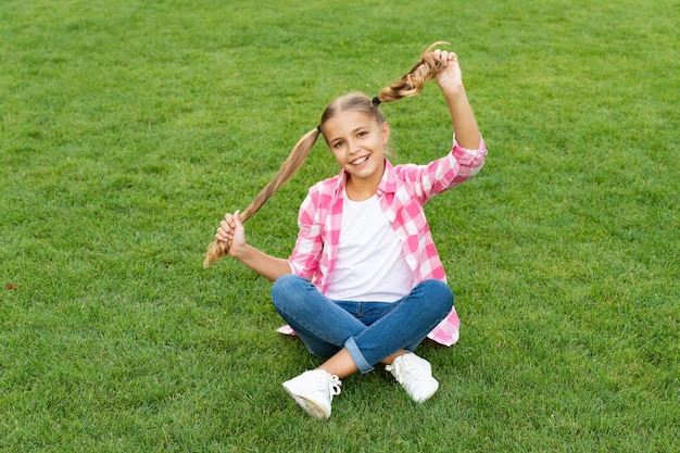 Positive teen child sit on green grass outdoor