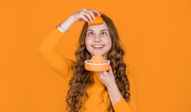 Positive teen girl hold orange and juicer on yellow background