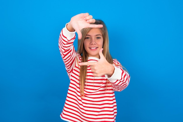 Positive teen girl with cheerful expression has good mood gestures finger frame actively at camera