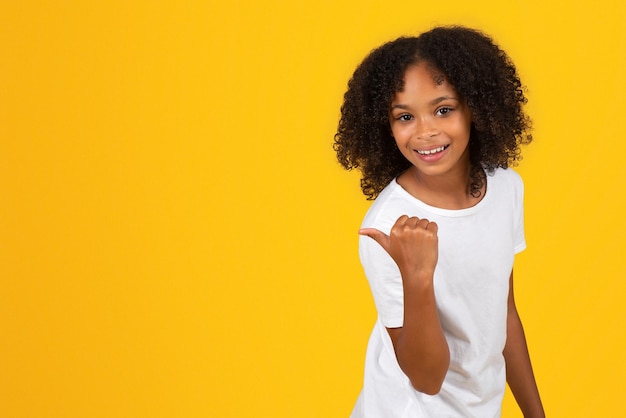 Positive teenage black pupil girl in white tshirt point finger on empty space recommends study
