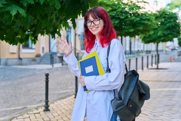 Studentessa adolescente positiva che guarda l'obbiettivo agitando la mano all'aperto