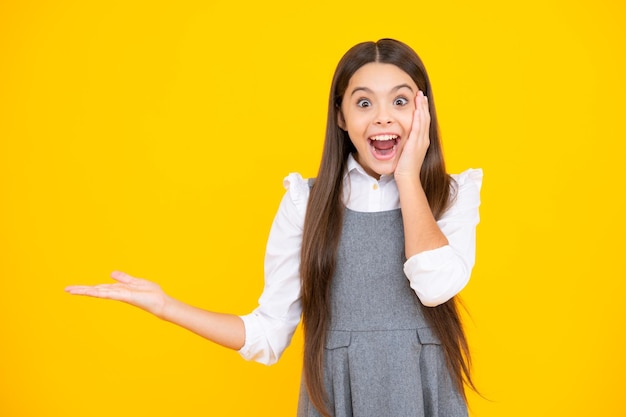 Positive teenager child points aside with cheerful expression shows amazing at blank empty space