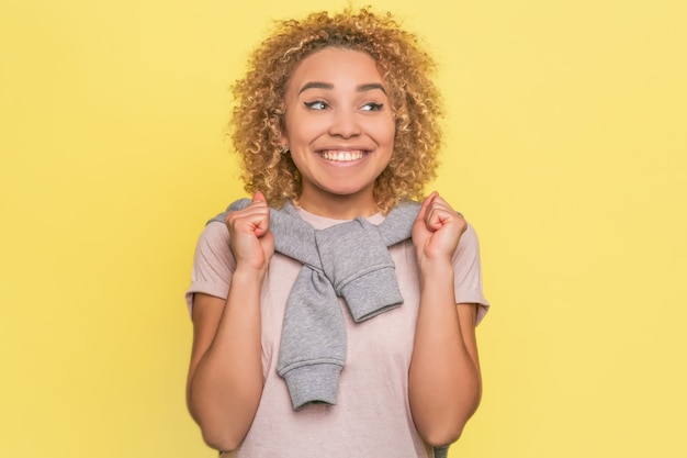 Photo positive and very happy girl is holding her hands in fists and smiling. she is looking aside. girl is full of hope.