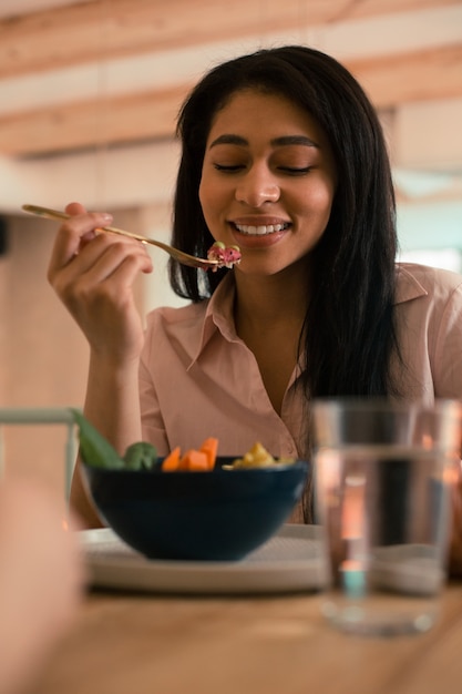 フォークから野菜サラダを食べながら笑顔で食事を見ているポジティブな女性