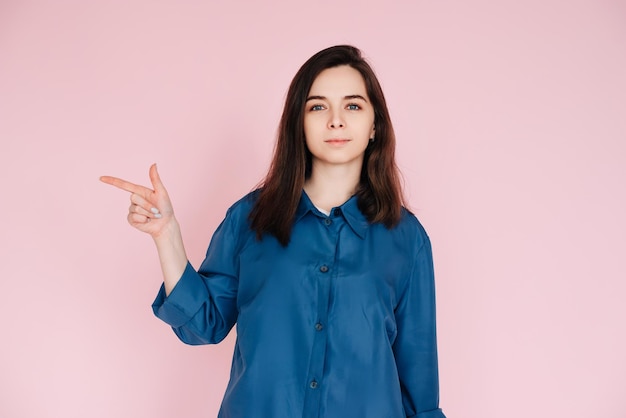 Positive woman pointing with finger sharing useful tips in empty space conceptual photo on pink