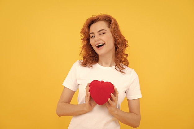 Positive woman presenting red heart on yellow background 14 february