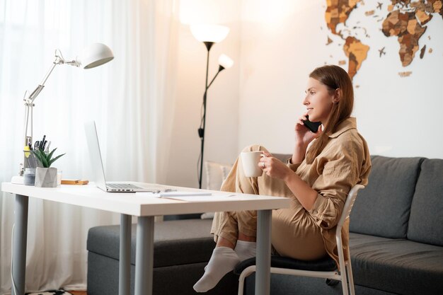 Positive woman speaking mobile and drinking morning coffee at\
table