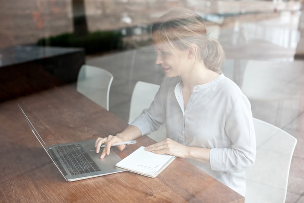 Positive woman using laptop and making notes