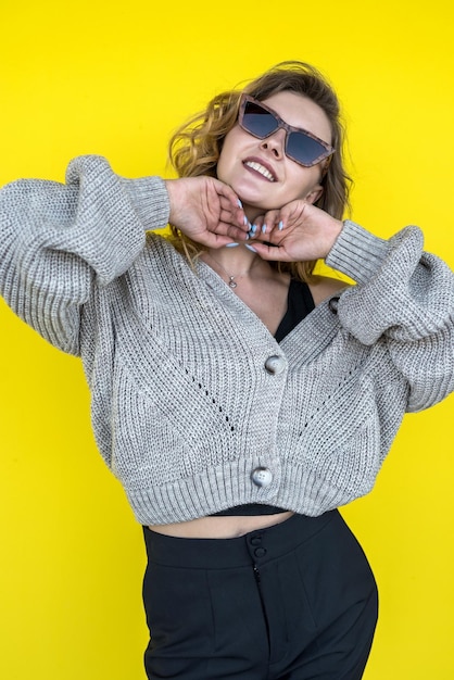 노란 벽에 격리된 따뜻한 회색 니트 겨울 스웨터를 입은 긍정적인 여성 아름다움과 감정 개념