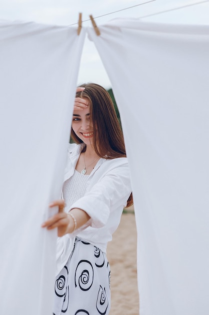 Positive woman in white clothing standing near white sheets on summer beach