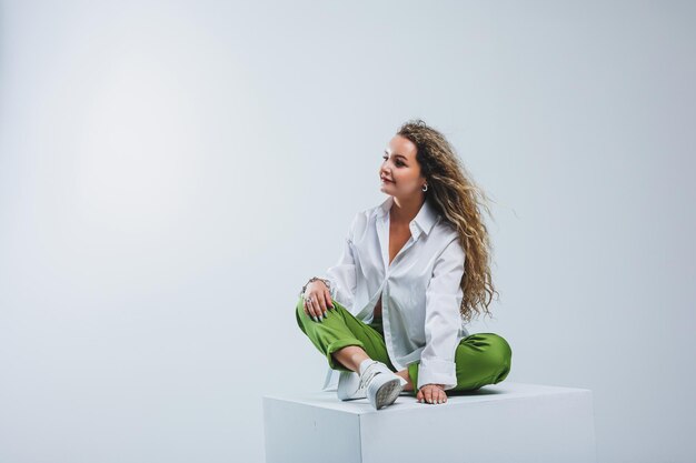 Positive woman with curly hair in a white light cotton shirt and trousers on a white isolated background Women's casual wear